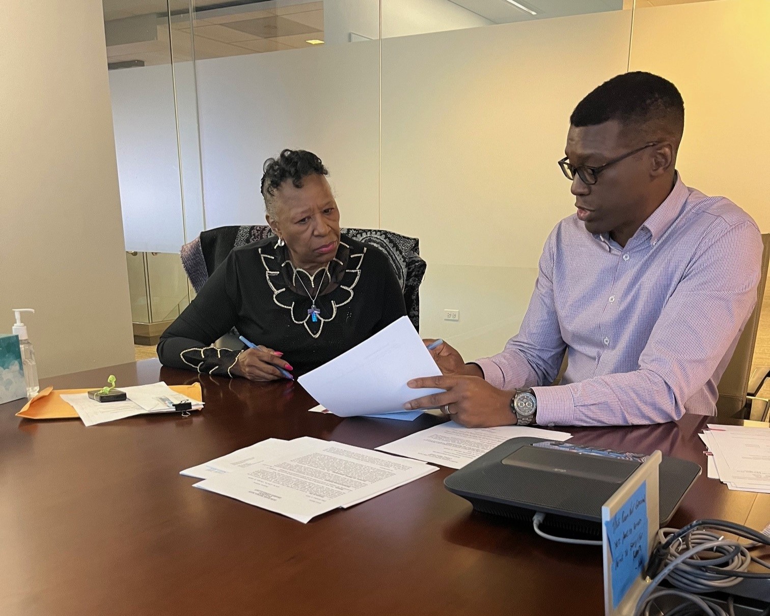 Man on right talking to woman on left. He is pointing to something on a paper, both holding pens