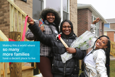 Three Black women smiling in front of a new Habitat Chicago home. Middle woman is holding a hammer and flowers