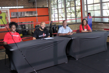 Four individuals sitting at a table inside a boxing ring